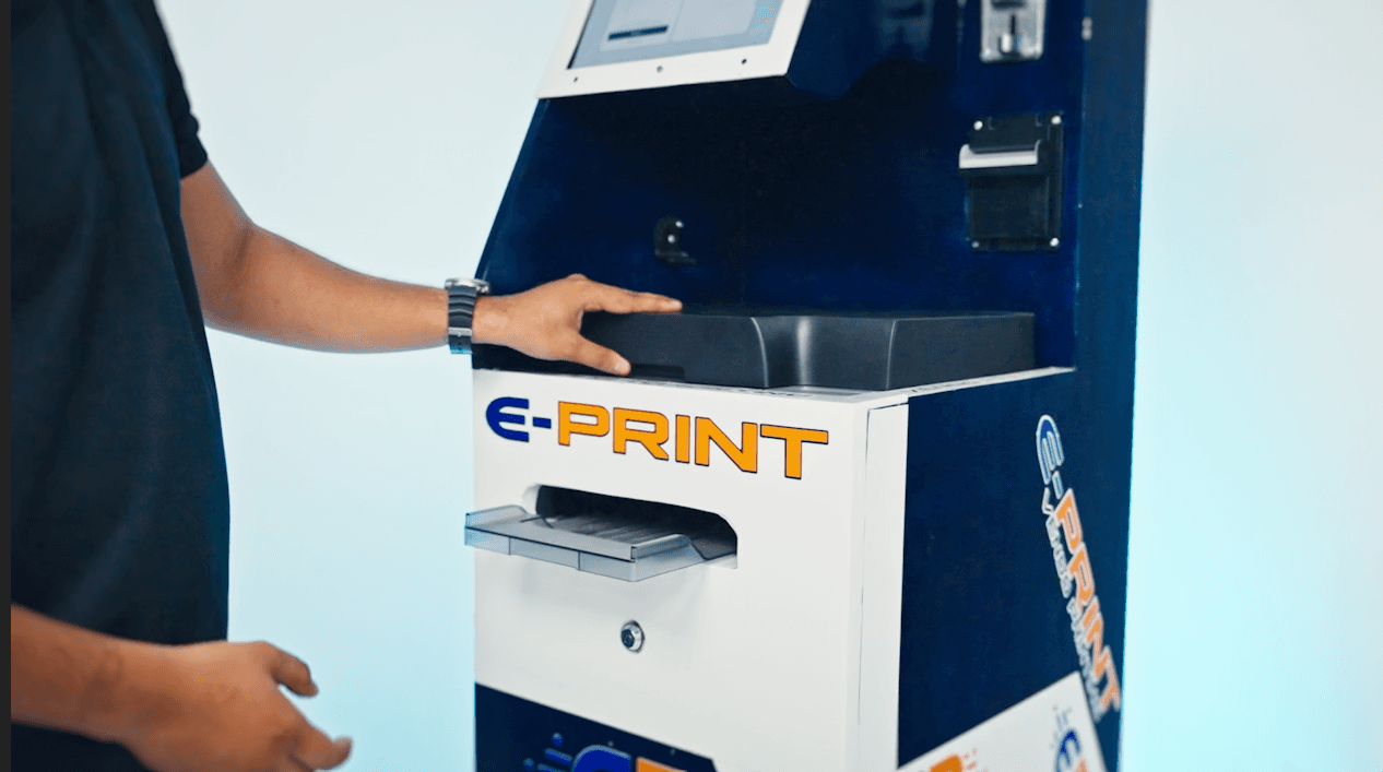 A person using the E-Print kiosk, resting a hand on its scanner cover
